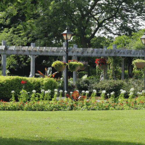 Green park with pergola, flowers, and lawn.